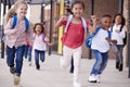 A group of smiling multi-ethnic school kids running in a walkway outside their infant school building after a lesson, close up Royalty Free Stock Photo