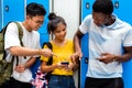 Group of smiling multiracial teen friends interacting using a smartphone in high school corridor