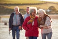 Group Of Smiling Senior Friends Walking Arm In Arm Along Shoreline Of Winter Beach Royalty Free Stock Photo