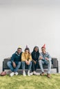 group of smiling young multiethnic friends in party hats sitting