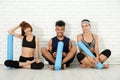 Group of sporty people with yoga mats sitting near white brick wall