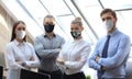 Group of successful business people in preventive masks during epidemy on the background of the office. Royalty Free Stock Photo