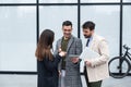 Group of successful young business people, leaders in marketing and motivation, stand in front of office building and consult