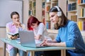 Group of teenage students study sitting at desk in library, in focus is guy using laptop