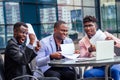 A group of their three successful African American businessmen in a stylish suit sit at the table and work with a laptop