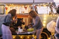 Group of three adult people friends celebrate and have dinner together in outdoor travel vacation with table food and vintage van