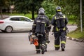A group of three brave firefighters walking along the street in uniform and with equipment. rear view, blurred