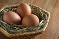 Three brown eggs lay on straw in a wicker basket. Baske