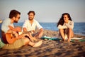 Group of three caucasian friends sitting at the beach, enjoying sunset, smiling