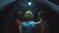 A group of three friends huddle together facing the darkened tent with a mix of fear and fascination on faces. .