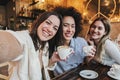 Group of three happy young women taking a selfie portrait on a coffee shop. Multi ethnic friends taking a photo smiling