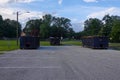 A group of three long blue dumpsters full of construction debris in a parking lot
