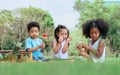 Group of three mixed race African and caucasian little cute kids sitting, playing in outdoor green park for picnic, eating fruit,