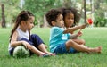 Group of three mixed race African and caucasian little cute kids sitting, playing in outdoor green park for picnic, eating fruit,