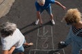 Group of three people playing together in the street on the asphalt at hopscotch - active seniors and woman having fun