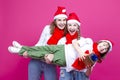 Group of Three Positive Caucasian Girls With Santa Hats Having Fun While Lifting Teenage Girl Holding Hands Closed Against Trendy Royalty Free Stock Photo