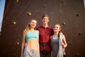 Group of three rock climbers with safety equipment smiling and looking at camera against artificial climbing wall Royalty Free Stock Photo