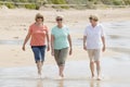 Group of three senior mature retired women on their 60s having fun enjoying together happy walking on the beach smiling playful