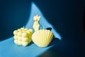 Group of three soy candles in the bubble cube, sea shell and Venus form in yellow pastel colors. Blue background.