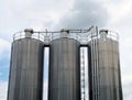 Group of three tall steel chemical storage tanks with connecting pipes and ladders against a blue cloudy sky