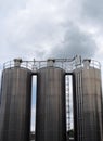 Three tall steel chemical storage tanks with connecting pipes and ladders against a blue cloudy sky Royalty Free Stock Photo