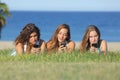 Group of three teenager girls typing on the mobile phone lying on the grass