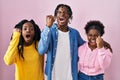 Group of three young black people standing together over pink background angry and mad raising fist frustrated and furious while