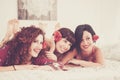 Group of three young cheerful women have fun together laying on the bed ready to go out for the night life - beauty and make up Royalty Free Stock Photo