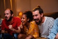 Group of three young friends sitting on the couch and watching sports on tv together at home screaming cheerful. Sports Royalty Free Stock Photo