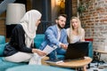 Group of three young mixed race people, muslim woman, caucasian man and woman, sitting together at the table with laptop Royalty Free Stock Photo