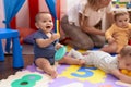 Group of toddlers playing with dish toy sitting on floor at kindergarten Royalty Free Stock Photo