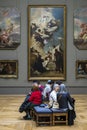 A group of tourists from all around the world sitting in the Louvre Museum