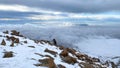 Group of tourists climbs uphill past red stones. Climbers with small backpacks and trekking poles are walking on a snowy slope.