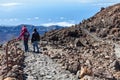 A group of tourists descend from the summit of the Teide volcano along a stone staircase among the lava heap. Three people in