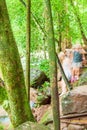A group of tourists hiking along a stream in tropical forest. Lush foliage, moss and lichen in the trunks and rocks. Kaeng Krachan