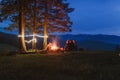A group of tourists sits around a campfire at a campsite. Lights and night in the mountains