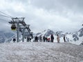 A group of tourists stands on the mountain at the lift and is photographed and admires the beautiful views of the snowy mountains