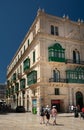 A group of tourists walk through the old town of Valetta in Malta. On the side the facade of a historical building with the Royalty Free Stock Photo