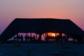 Group of tourists watching colorful sunset under shelter. Tourist resort in Africa. Backlight, silhouette, rear view