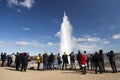 Group of tourists watching and taking pictures of the Strokkur geyser erupting