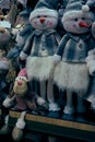 A group of toy snowmen with a red carrot nose, dressed in checkered jackets and hats with a dog, stand on a store shelf