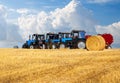 group of tractors with tractor drivers on a field harvested with wheat and round haystacks