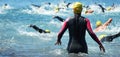 Group triathlon participants running into the water for swim