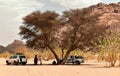 A group of Tuareg men with jeeps rest under a tree with the rocky Sahara Desert in the background, Djanet, Algeria, Africa Royalty Free Stock Photo