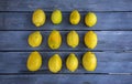 A group of twelve lemons arranged in a square pattern on a gray wood table