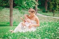Group of two people, white Caucasian mother and baby girl child in white dress sitting playing in green summer park forest outside