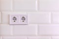 Group of two white european electrical outlets on a wall of white tile in a modern kitchen or bathroom