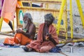 A Group of unidentified Sadhus pilgrims dressed in orange clothes, sitting in the street, on the road, waiting for food. It is a m