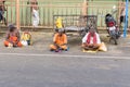 A Group of unidentified Sadhus pilgrims dressed in orange clothes, sitting in the street, on the road, waiting for food. It is a m