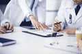 Group of unknown doctors are sitting at the desk and discussing medical treatment, using a clipboard, close-up. Team of